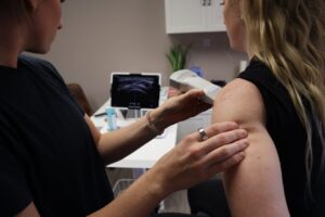 Ultrasound therapy being performed on a patient shoulder by a medical professional in a clinic setting