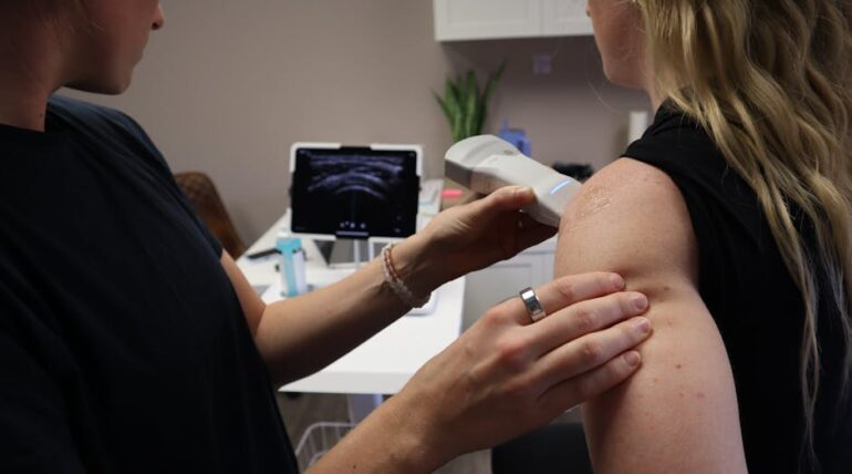 Ultrasound therapy being performed on a patient shoulder by a medical professional in a clinic setting